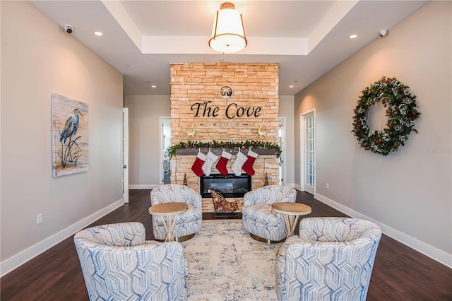 living area featuring a tray ceiling, dark hardwood / wood-style flooring, and a stone fireplace