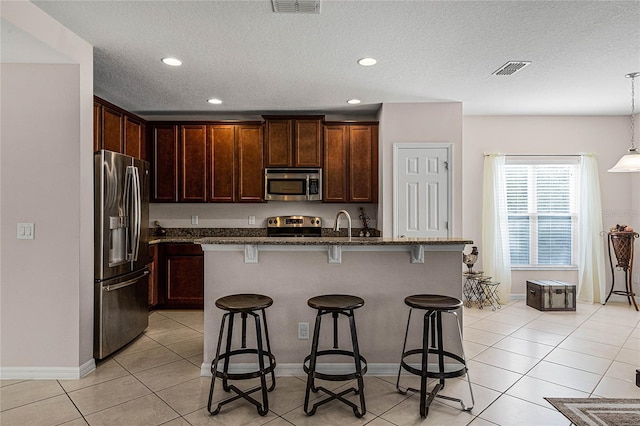 kitchen with a kitchen breakfast bar, stainless steel appliances, hanging light fixtures, and an island with sink