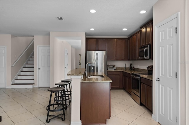 kitchen featuring a kitchen bar, light stone countertops, stainless steel appliances, sink, and an island with sink