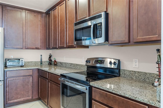 kitchen featuring light tile patterned flooring, light stone counters, and stainless steel appliances