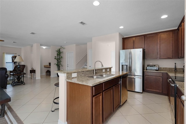 kitchen with sink, light tile patterned floors, an island with sink, appliances with stainless steel finishes, and a breakfast bar area