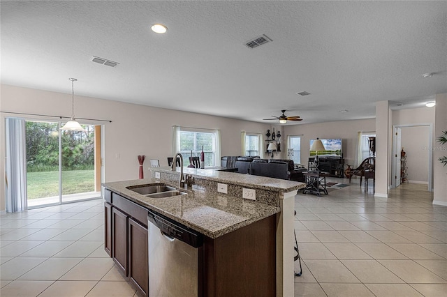 kitchen with light stone countertops, stainless steel dishwasher, sink, decorative light fixtures, and an island with sink