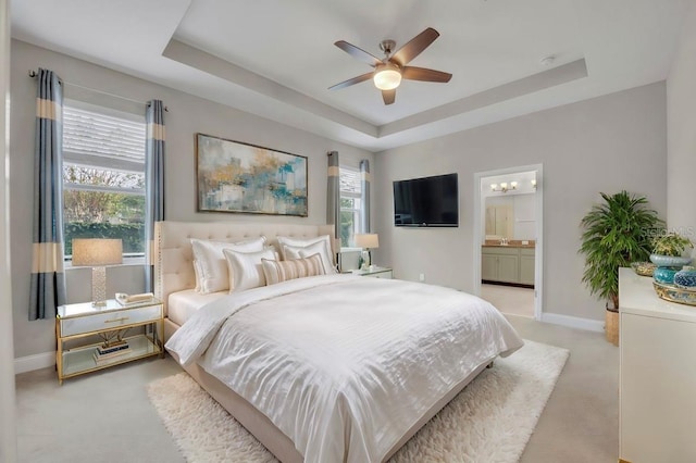 bedroom with ceiling fan, ensuite bathroom, light colored carpet, and a raised ceiling