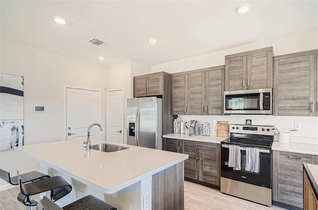 kitchen with sink, an island with sink, light hardwood / wood-style floors, a breakfast bar, and appliances with stainless steel finishes