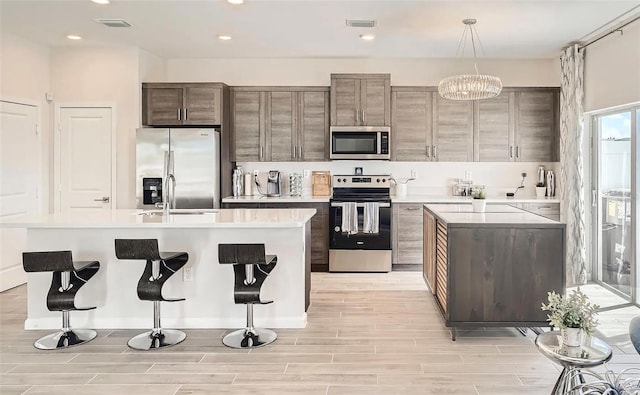 kitchen with a kitchen island with sink, stainless steel appliances, decorative light fixtures, and a notable chandelier