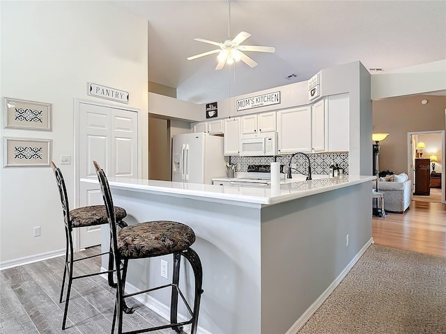 kitchen with white appliances, white cabinetry, a kitchen breakfast bar, tasteful backsplash, and kitchen peninsula