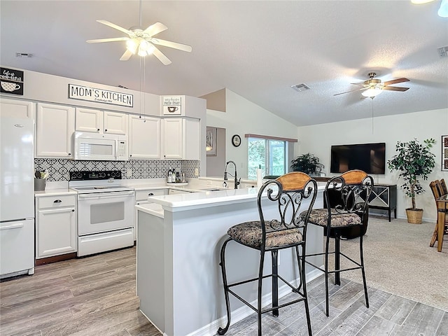 kitchen with white appliances, a breakfast bar area, kitchen peninsula, and white cabinets