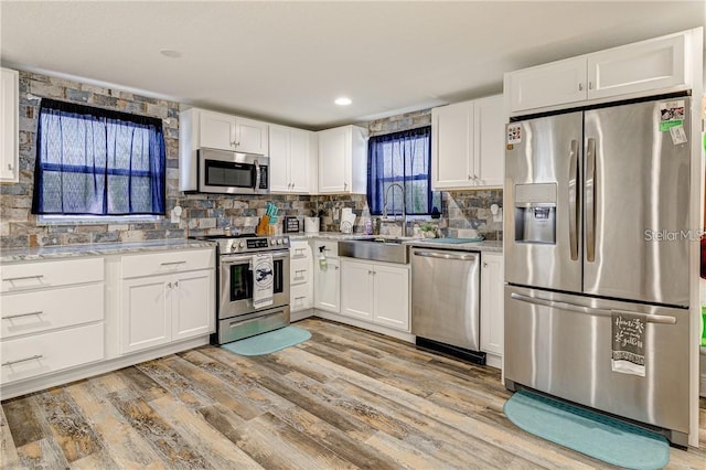 kitchen with white cabinets, sink, tasteful backsplash, light hardwood / wood-style floors, and stainless steel appliances