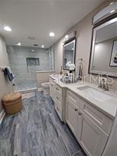 bathroom with toilet, vanity, wood-type flooring, and tiled shower