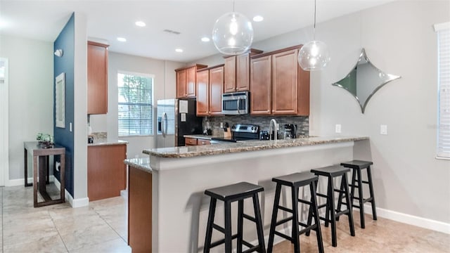 kitchen featuring kitchen peninsula, decorative backsplash, light stone counters, stainless steel appliances, and hanging light fixtures