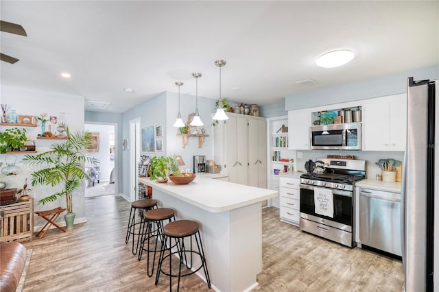 kitchen featuring light wood-type flooring, white cabinetry, stainless steel appliances, and hanging light fixtures