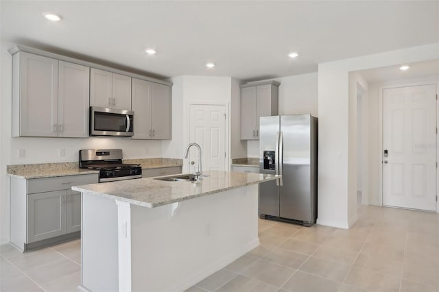 kitchen with appliances with stainless steel finishes, light stone counters, a kitchen island with sink, sink, and light tile patterned floors