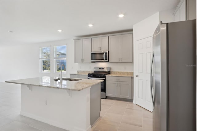 kitchen with a kitchen island with sink, sink, light stone countertops, appliances with stainless steel finishes, and a kitchen bar