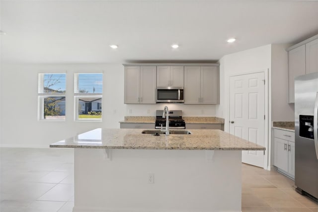 kitchen with a center island with sink, a kitchen breakfast bar, sink, light stone countertops, and stainless steel appliances