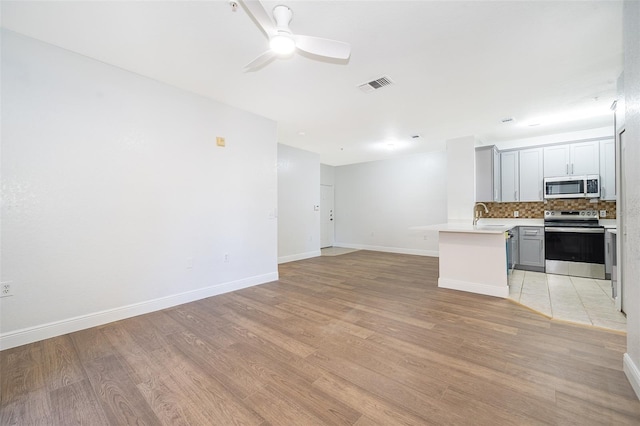 kitchen with decorative backsplash, light wood-type flooring, stainless steel appliances, ceiling fan, and gray cabinets