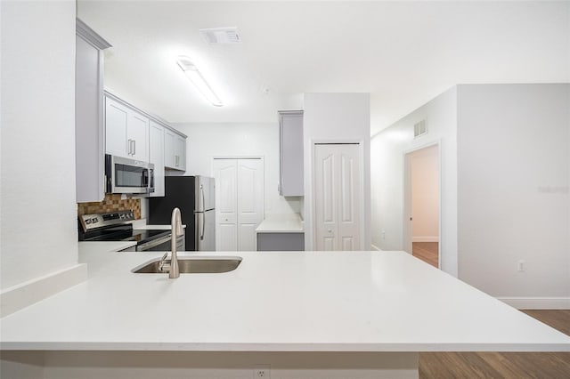 kitchen featuring sink, appliances with stainless steel finishes, tasteful backsplash, dark hardwood / wood-style flooring, and kitchen peninsula