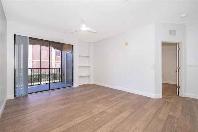 spare room with built in shelves, ceiling fan, and wood-type flooring