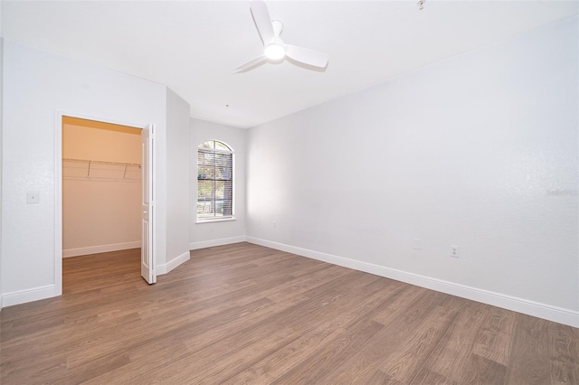 unfurnished bedroom featuring a walk in closet, ceiling fan, a closet, and hardwood / wood-style flooring