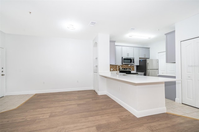 kitchen featuring gray cabinets, light hardwood / wood-style floors, kitchen peninsula, and appliances with stainless steel finishes