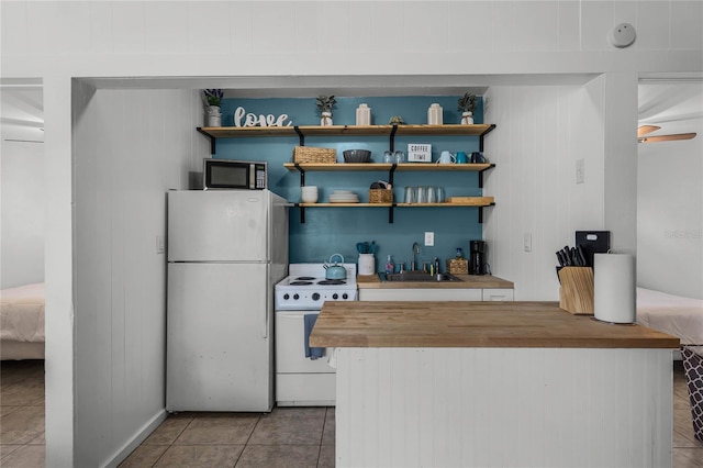 kitchen featuring white appliances, sink, wooden walls, ceiling fan, and light tile patterned floors