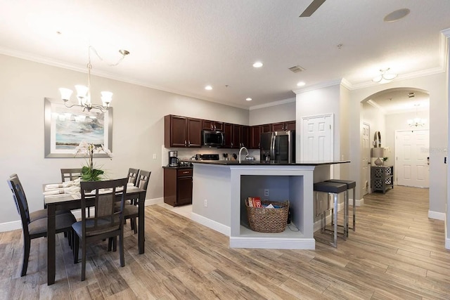 kitchen with a center island with sink, light wood-type flooring, crown molding, and appliances with stainless steel finishes