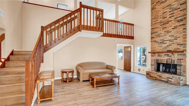 living room featuring a towering ceiling, light hardwood / wood-style floors, and a brick fireplace