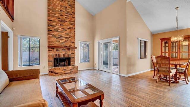 living room featuring a brick fireplace, a notable chandelier, high vaulted ceiling, and light hardwood / wood-style flooring