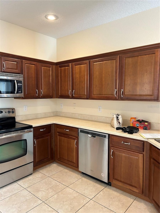 kitchen featuring light tile patterned flooring, a textured ceiling, and appliances with stainless steel finishes