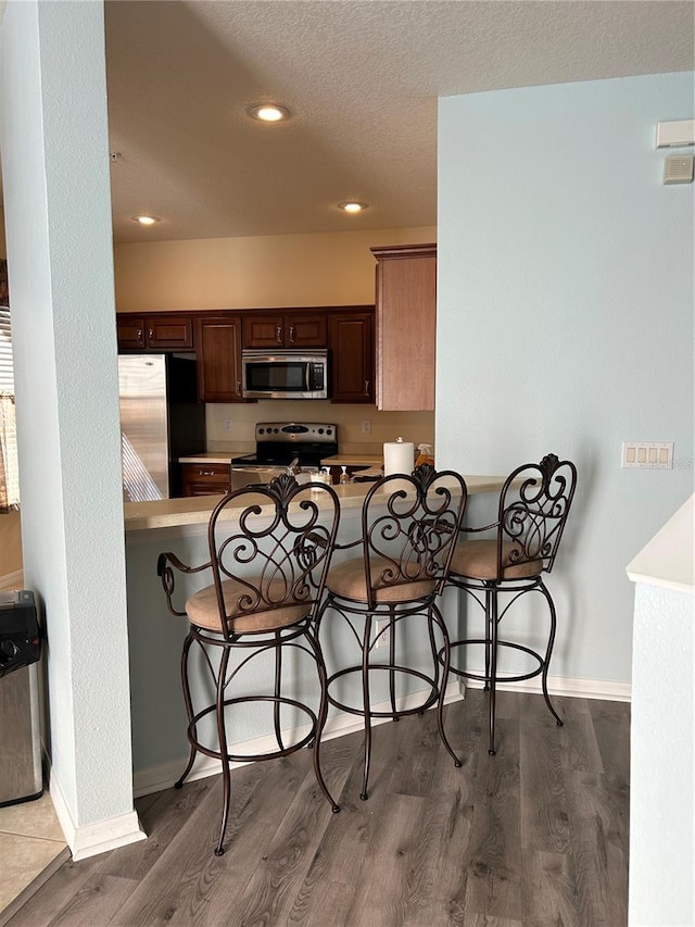 kitchen featuring a breakfast bar area, kitchen peninsula, hardwood / wood-style flooring, and appliances with stainless steel finishes