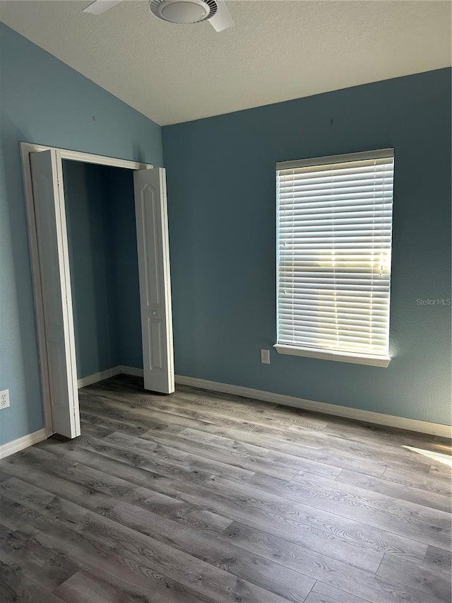 unfurnished bedroom featuring ceiling fan, a textured ceiling, lofted ceiling, a closet, and hardwood / wood-style flooring