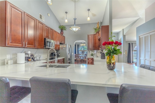 kitchen with sink, hanging light fixtures, light stone countertops, appliances with stainless steel finishes, and kitchen peninsula