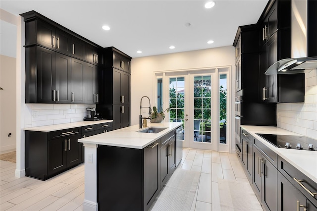 kitchen featuring decorative backsplash, french doors, a center island with sink, and wall chimney range hood