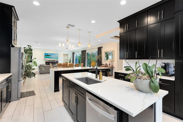 kitchen with sink, a notable chandelier, an island with sink, decorative light fixtures, and appliances with stainless steel finishes