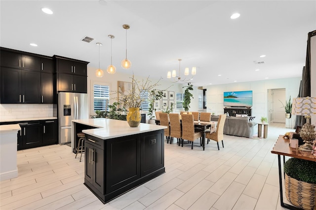 kitchen featuring decorative backsplash, stainless steel fridge, pendant lighting, an inviting chandelier, and a center island