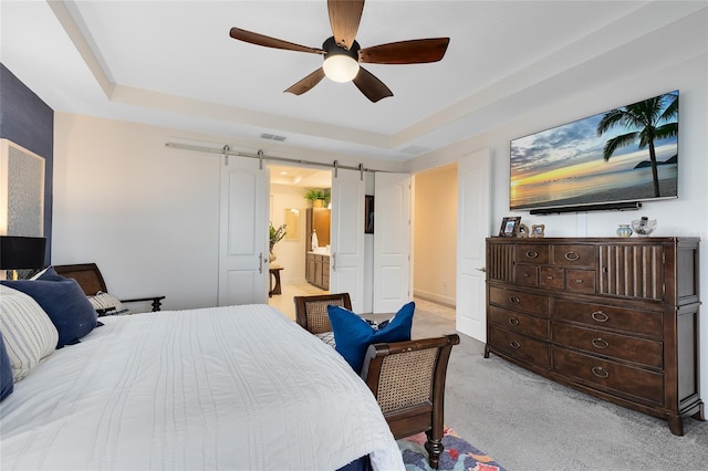 bedroom with ensuite bath, ceiling fan, a barn door, a tray ceiling, and light carpet