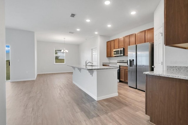 kitchen with light stone countertops, appliances with stainless steel finishes, light hardwood / wood-style floors, and hanging light fixtures