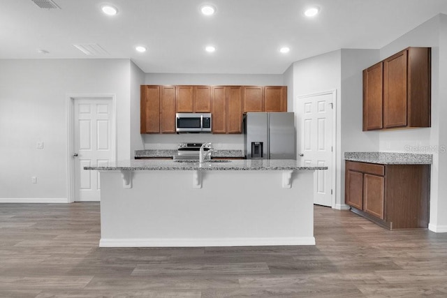 kitchen featuring hardwood / wood-style floors, a breakfast bar, a kitchen island with sink, and appliances with stainless steel finishes