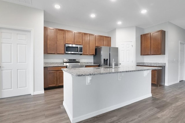 kitchen with a kitchen island with sink, a breakfast bar, wood-type flooring, and appliances with stainless steel finishes