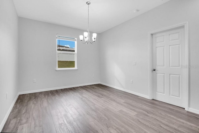 empty room with light hardwood / wood-style floors and an inviting chandelier