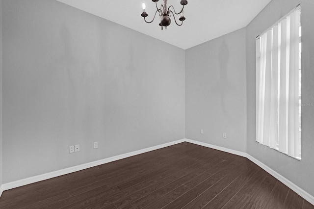 spare room featuring a chandelier and dark wood-type flooring