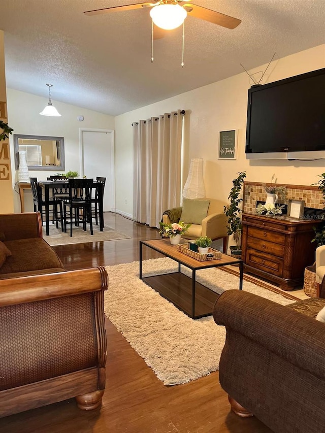 living room featuring lofted ceiling, ceiling fan, wood-type flooring, and a textured ceiling