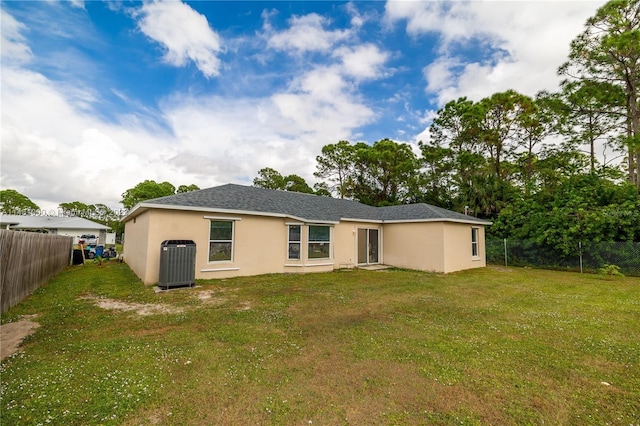 rear view of property with central air condition unit and a yard