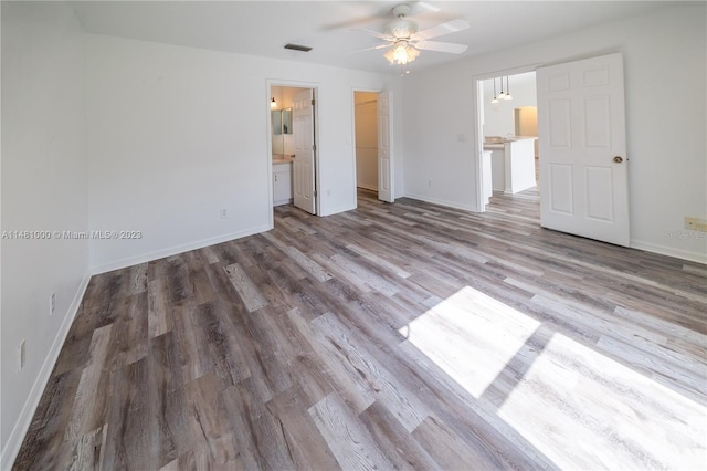 unfurnished bedroom featuring hardwood / wood-style floors, a walk in closet, ensuite bathroom, and ceiling fan