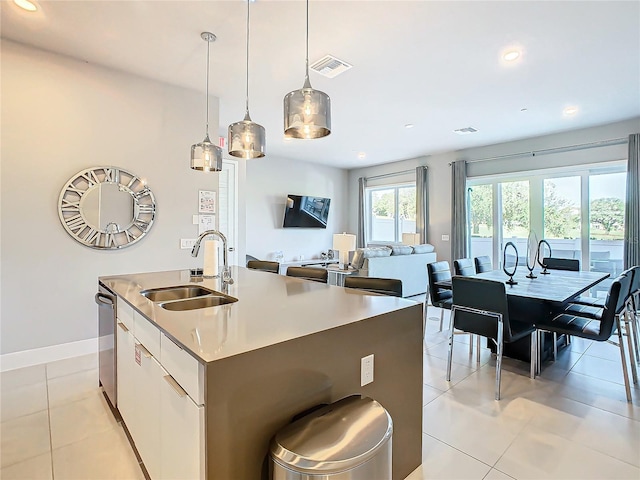 kitchen with sink, light tile patterned floors, a center island with sink, dishwasher, and hanging light fixtures