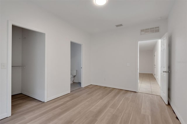 unfurnished bedroom with ensuite bathroom, a walk in closet, a closet, and light hardwood / wood-style flooring