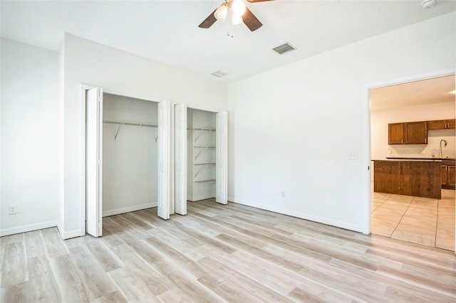 unfurnished bedroom featuring sink, light hardwood / wood-style flooring, ceiling fan, connected bathroom, and two closets