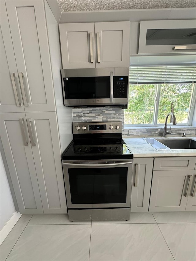 kitchen with sink, stainless steel appliances, light tile patterned floors, a textured ceiling, and white cabinets