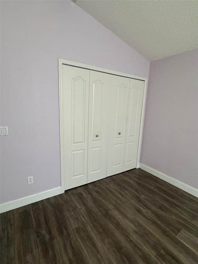 unfurnished bedroom featuring a textured ceiling, dark hardwood / wood-style floors, vaulted ceiling, and a closet