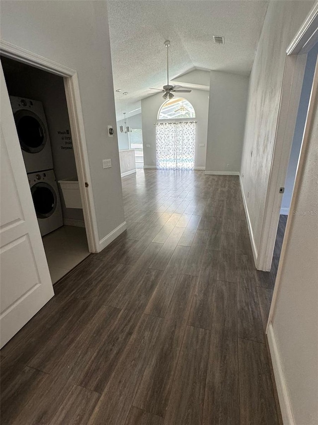 interior space featuring ceiling fan, dark hardwood / wood-style floors, stacked washer and dryer, a textured ceiling, and vaulted ceiling