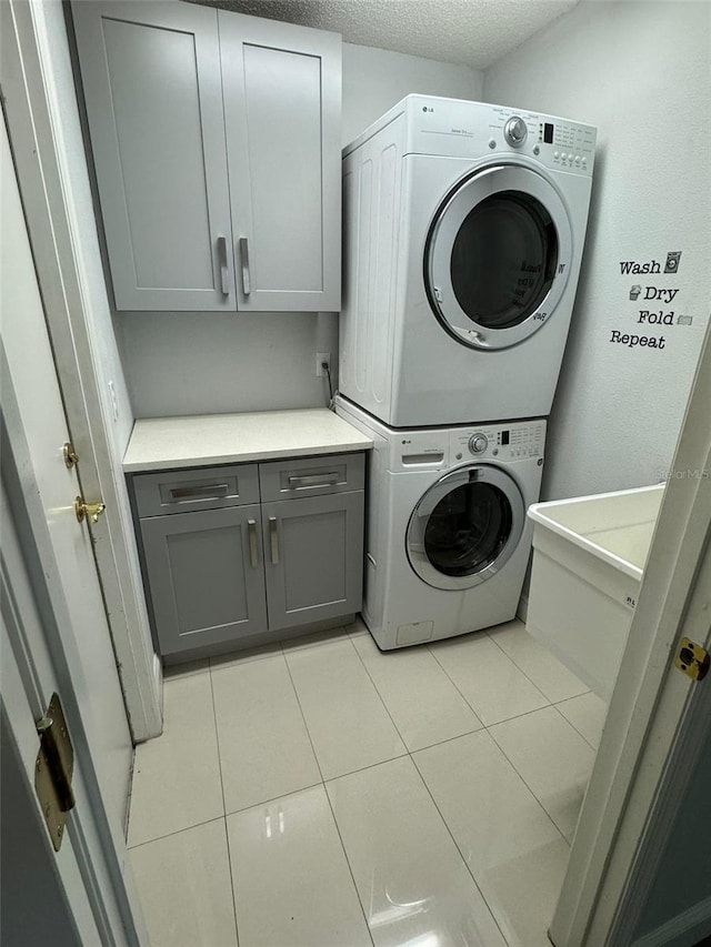 washroom with cabinets, light tile patterned floors, a textured ceiling, and stacked washing maching and dryer